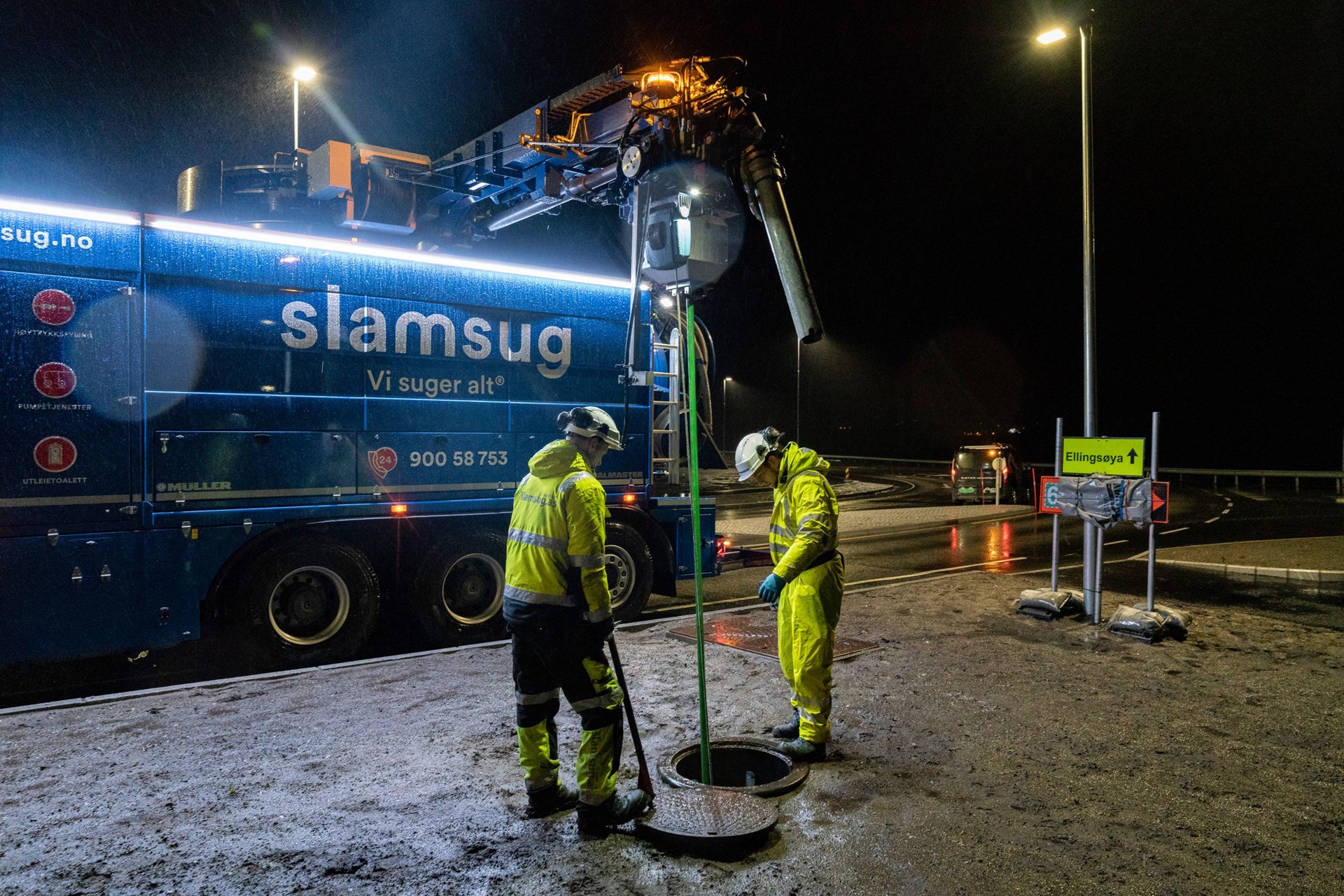 To personer som står over et kumlokk hvor det suges opp slam